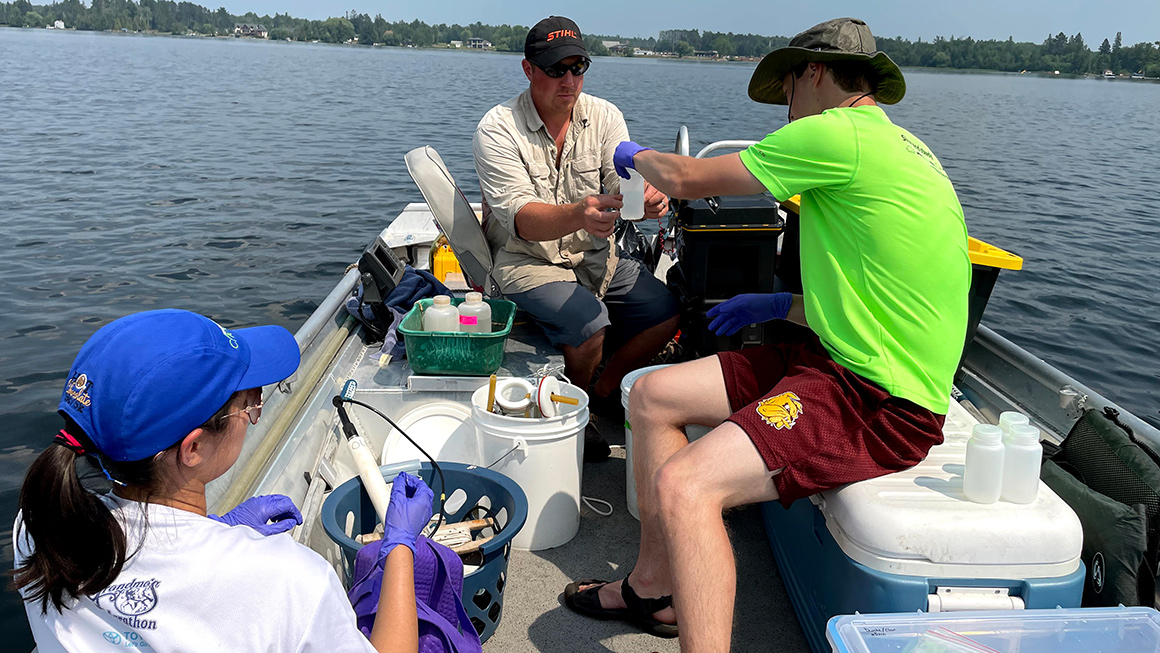 Freshwater sample collection by three researchers in a boat. 