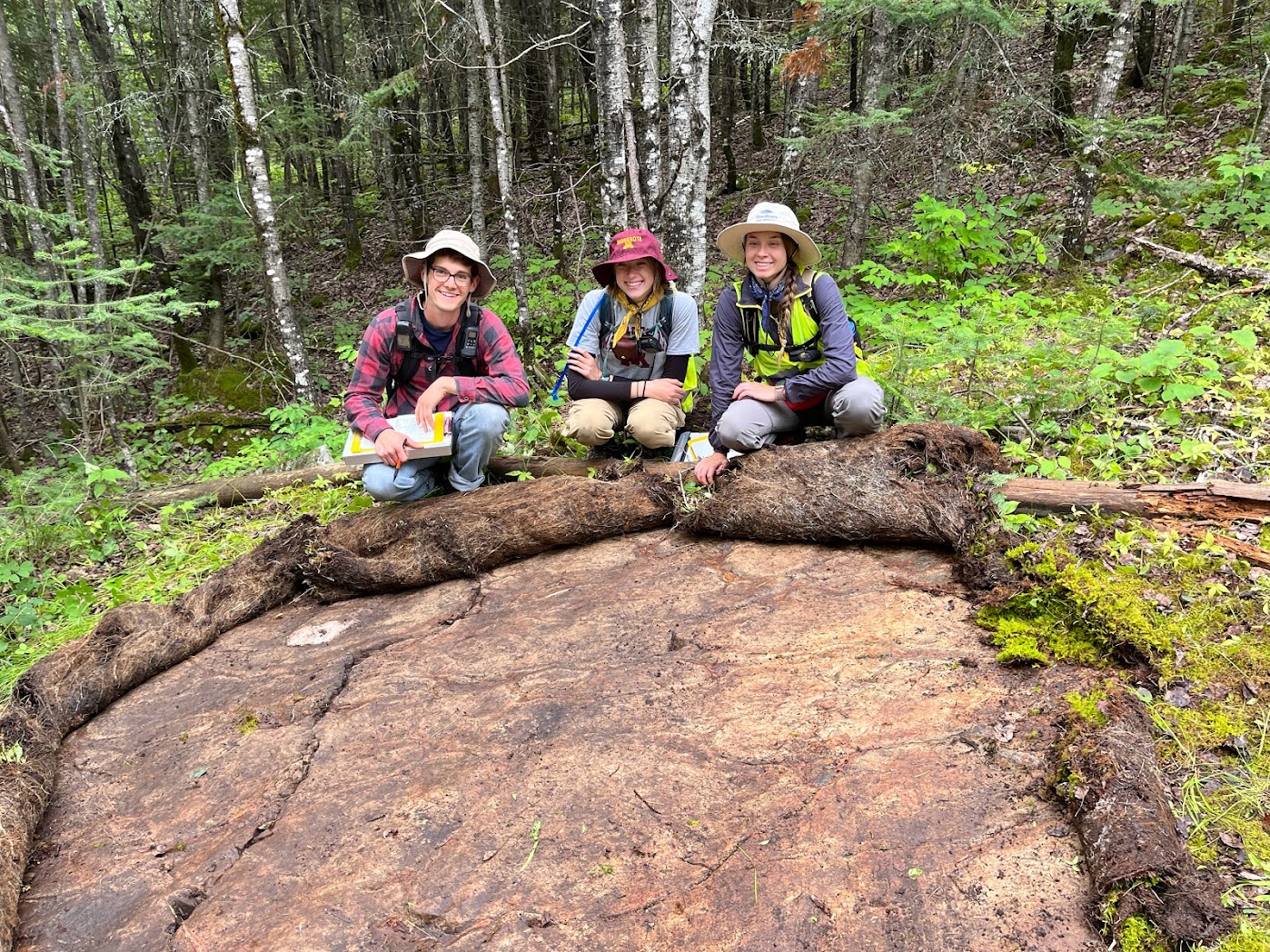 Three people crouch smiling on far side of a rock outcrop