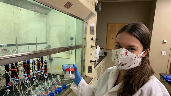 A woman in a white lab coat and gloves works in a laboratory.