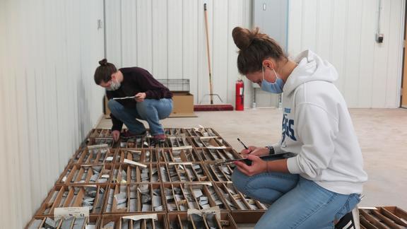 Students sit on floor looking at drill core samples in boxes.