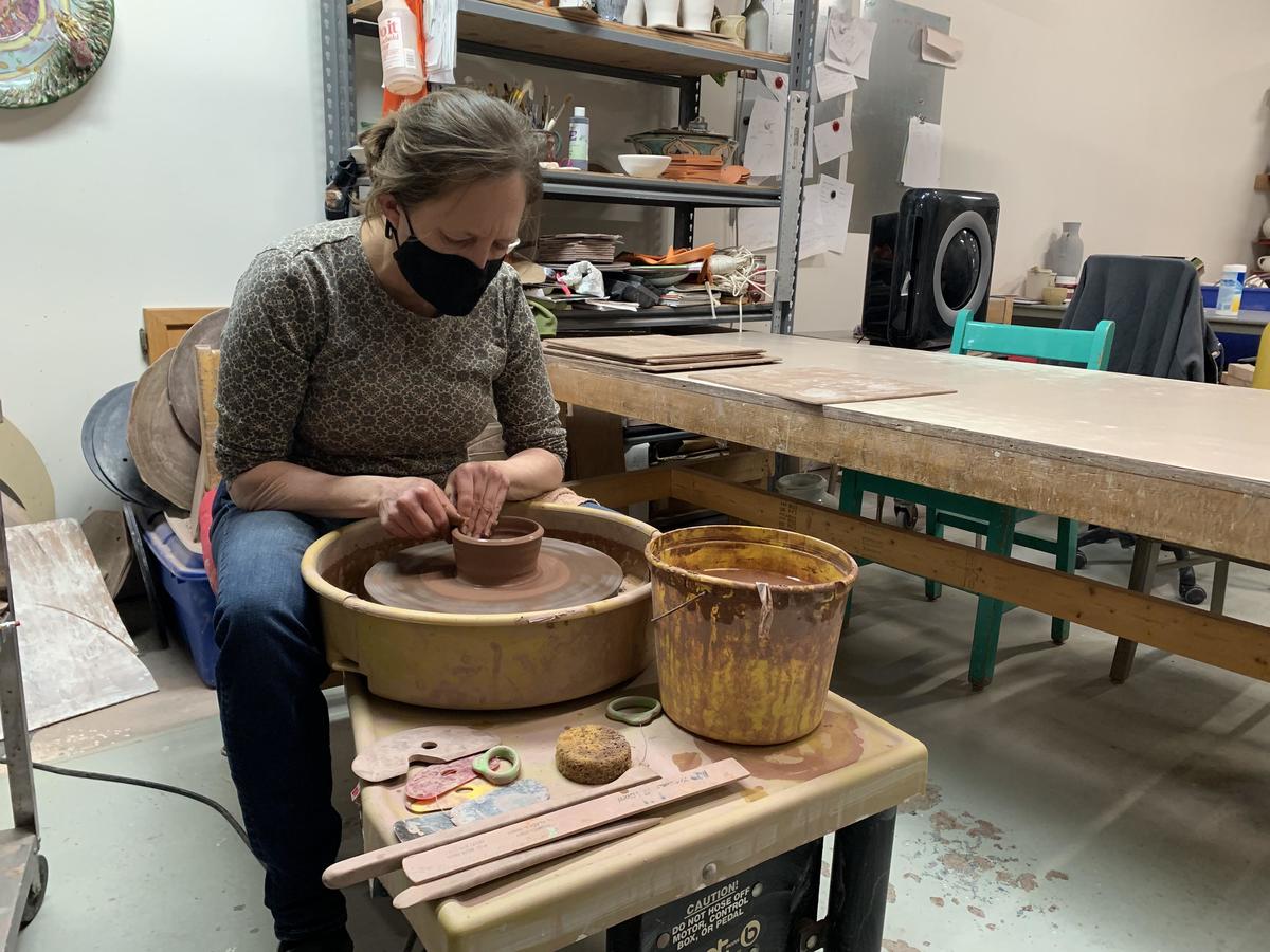 A woman is turning a clay bowl on a potters wheel
