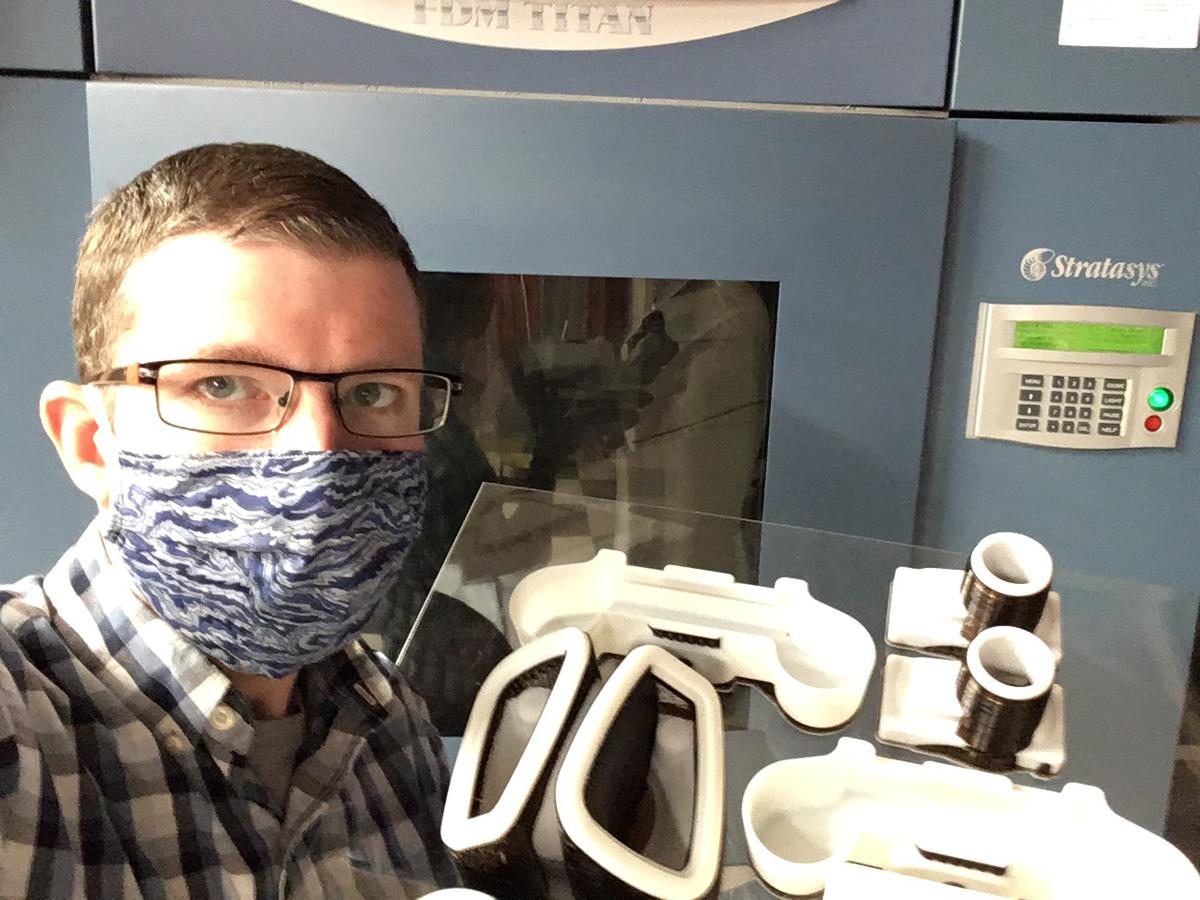 Man wearing face mask stands in front of machine with plastic parts visible