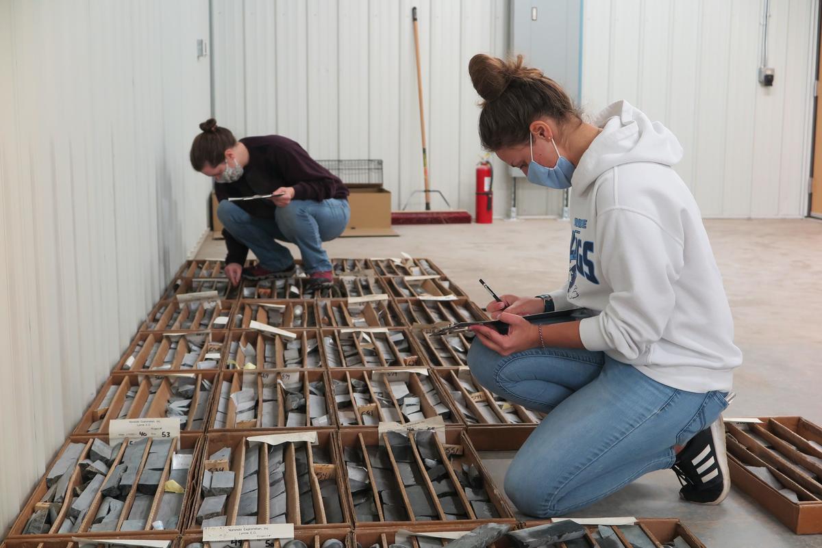 Students sit on floor looking at drill core samples in boxes.