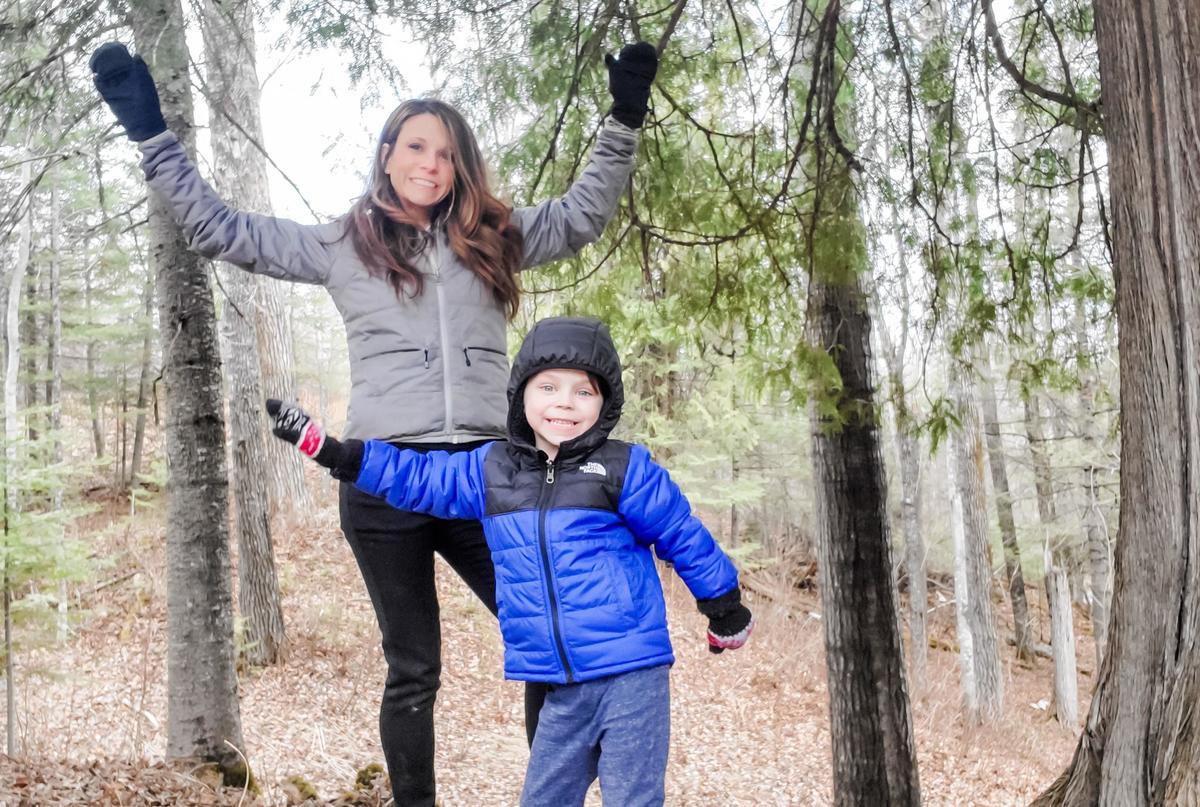 A woman and small boy throw hands in the air outdoors.
