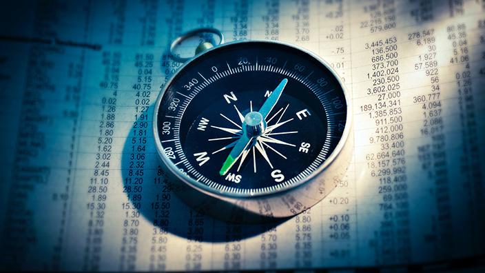 Compass on a background spreadsheet of financial numbers. 