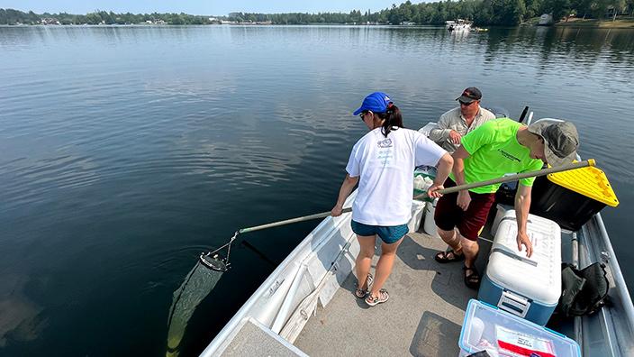 Three researchers aboard a boat sample for phytoplankton with a net. 