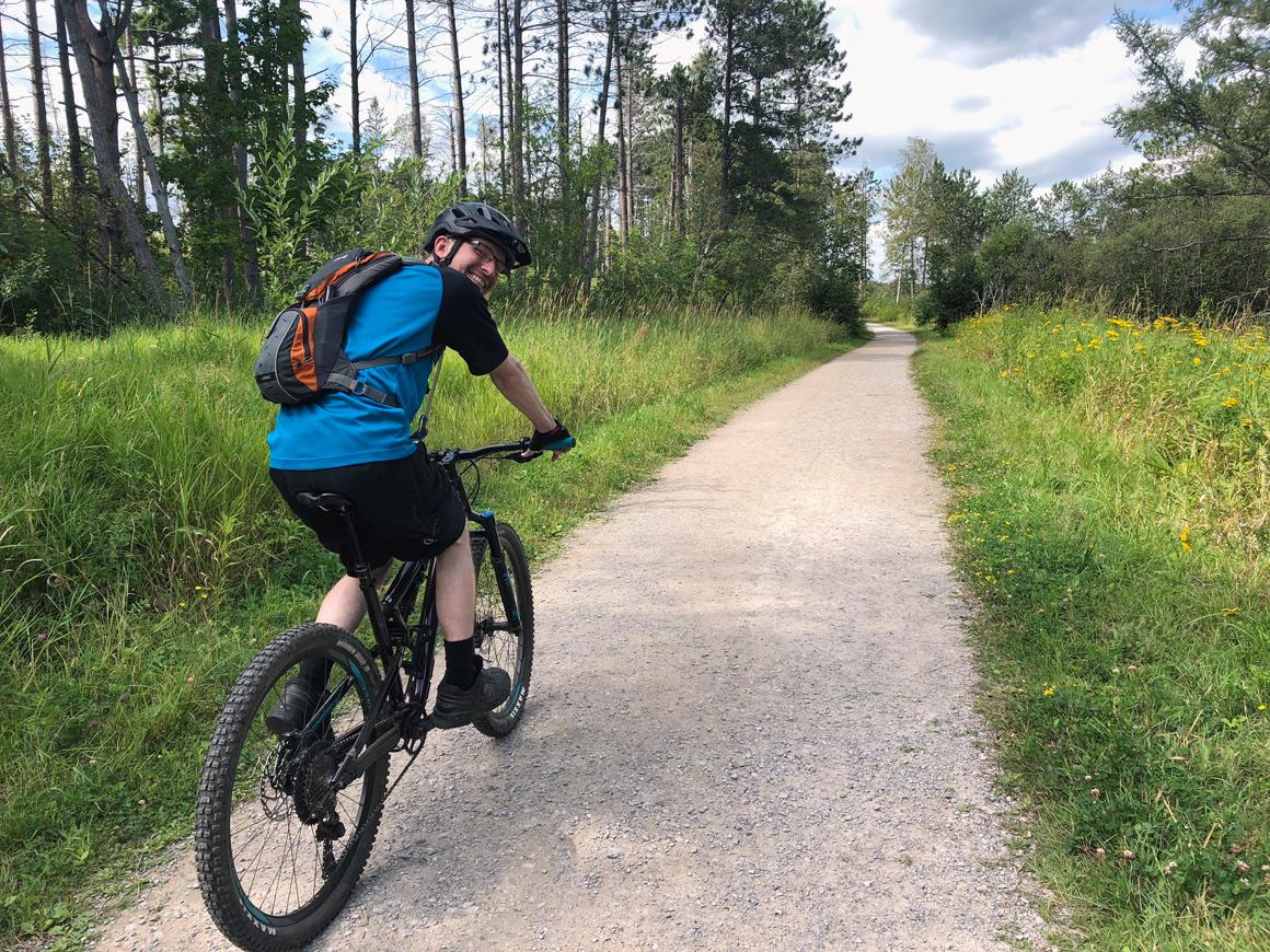 Kory Jenkins on Mountain Bike on gravel trail in forest.