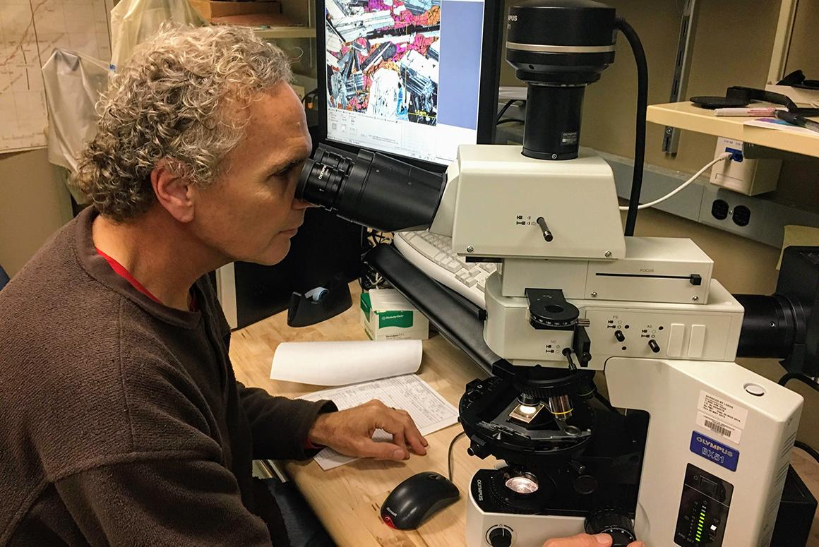 Researcher looking through microscope at a mineral sample. 