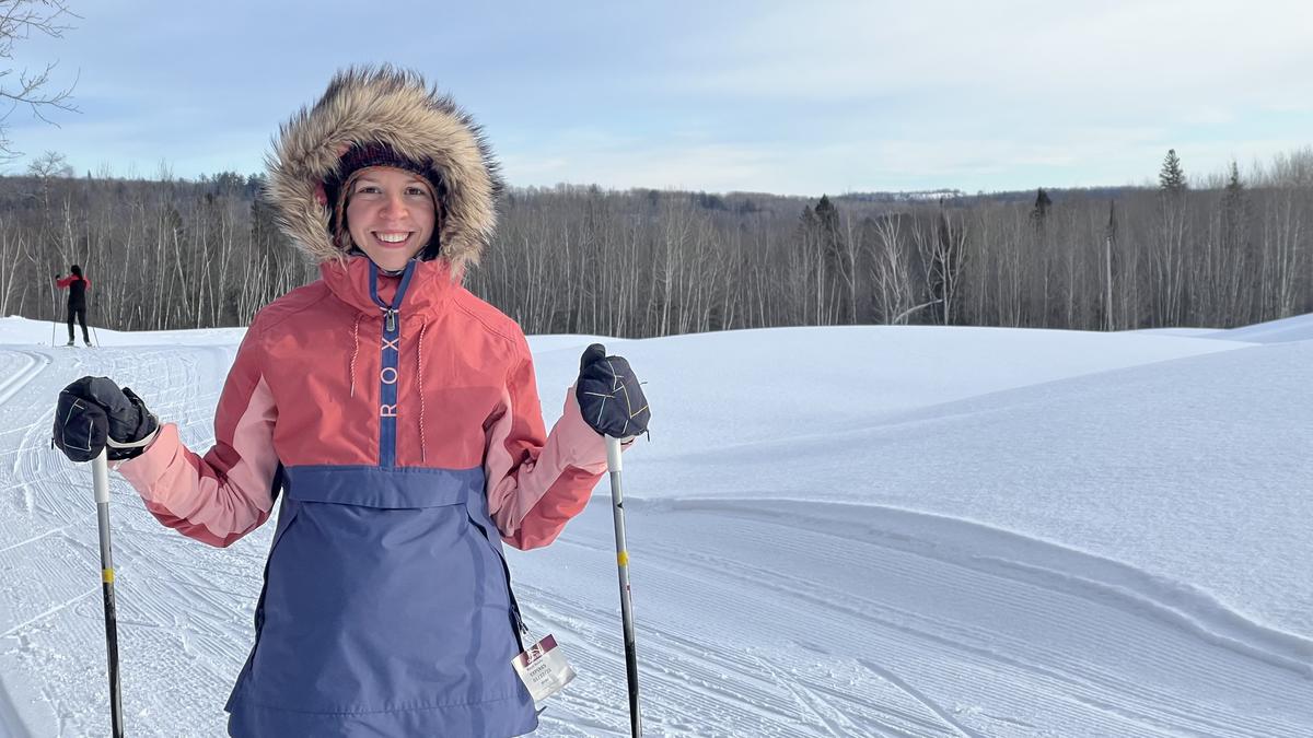 Woman outdoors in snowy scene in winter parka holds two ski poles