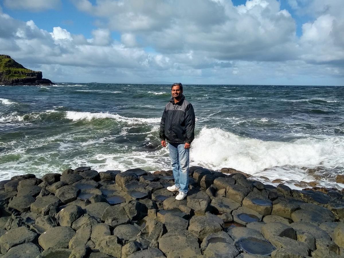 Man stands on a rocky shore with ocean in background.