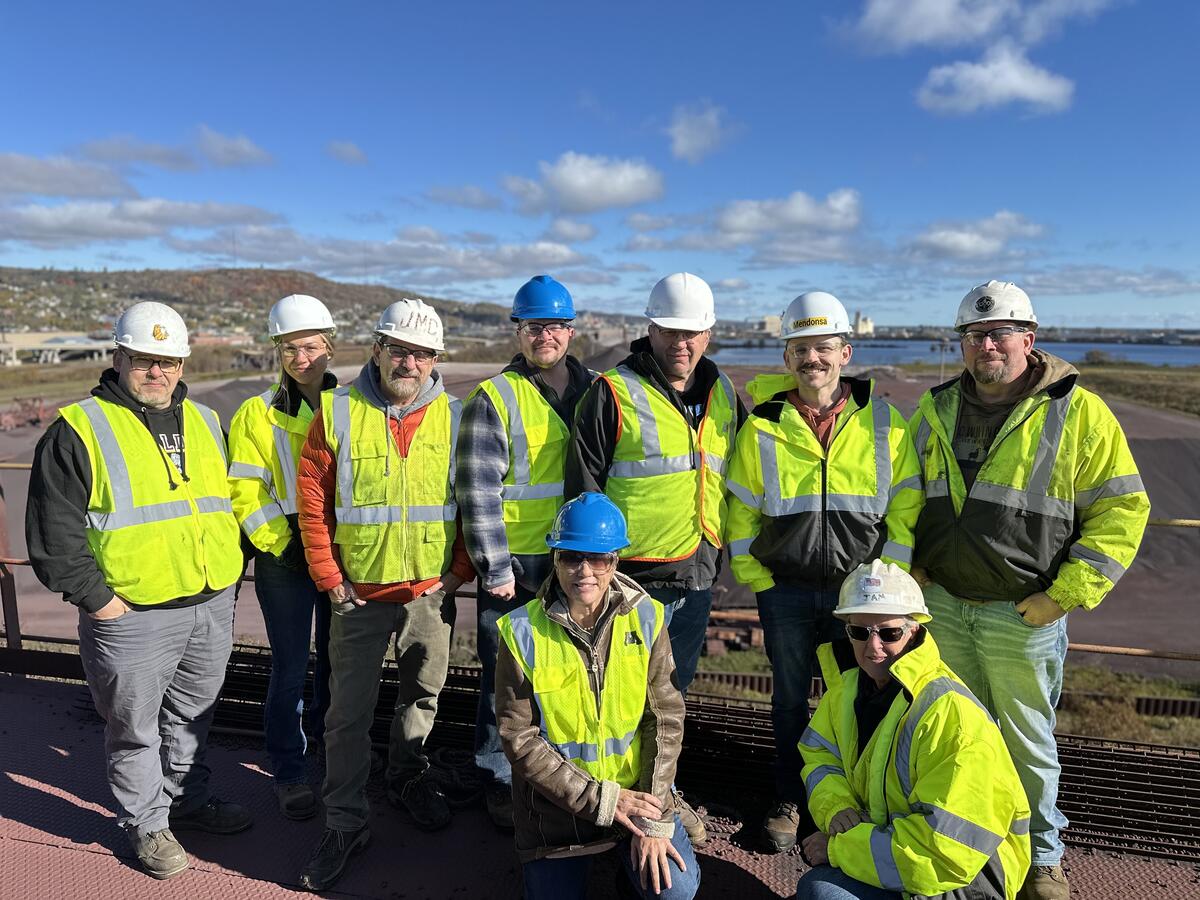 A group of nine people in safety PPE pose for a photo outdoors.