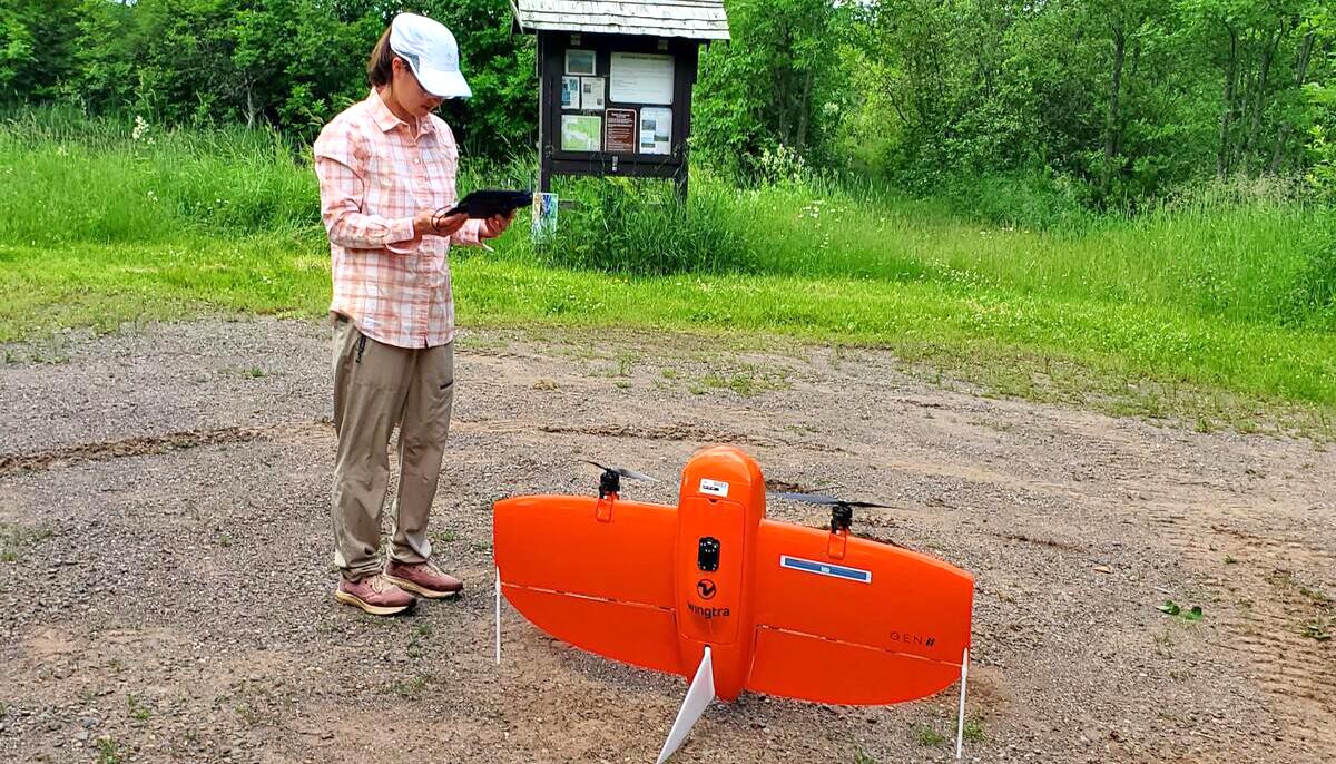 Woman stands before a red drone preparing for takeoff. 