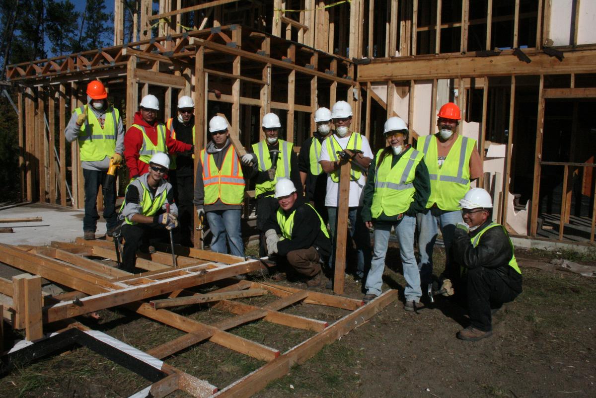 A dozen men in construction attire pose in front of a partially constructed structure.