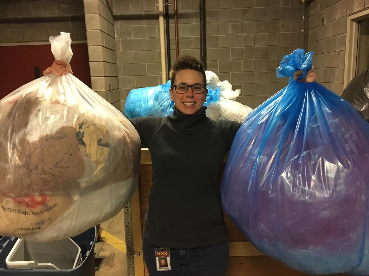 Woman smiles while holding two large bags filled with plastic.