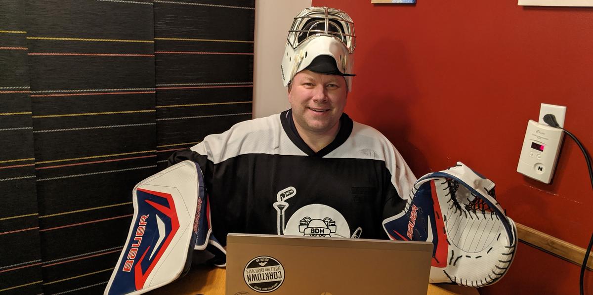 Man dressed in hockey gear stands behind a lap top computer