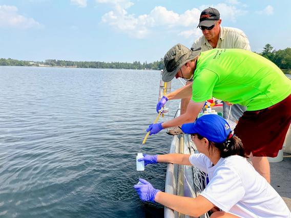 Three researchers take water sample from lake. 