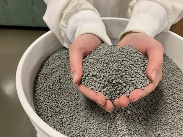 Two hands holding handfuls of small pellets over bucket