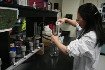 Woman in white lab coat pours water into a vial.