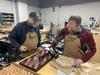 Two men at a wood shop workbench focused on tabletop project.