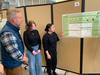 A man listens to two females at a poster presentation.